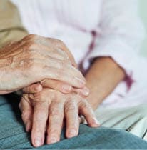 Close up of elderly hands of couple sitting on the sofa at home. Family and relationships concept